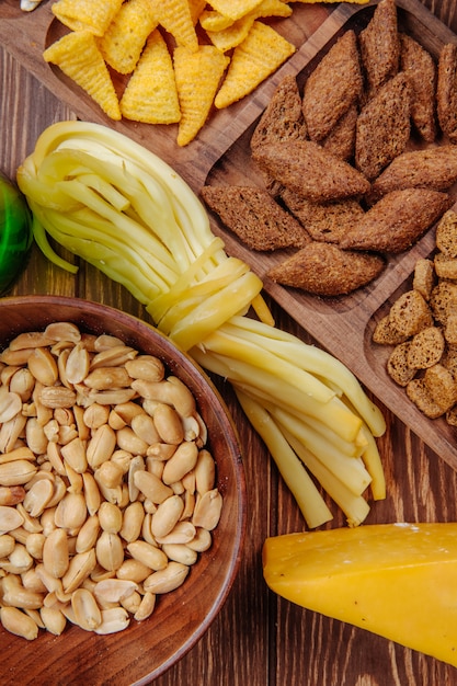 Vista superiore del formaggio a corde salato dei cracker del pane dei coni del cereale degli spuntini della birra e delle arachidi salate su legno rustico