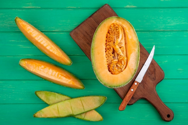 Vista superiore del melone cantalupo diviso in due su un bordo di legno della cucina con il coltello su superficie di legno verde