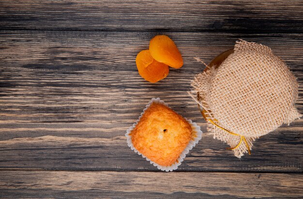 Vista superiore del muffin con albicocche secche e marmellata di pesche in un barattolo di vetro su legno rustico con spazio di copia