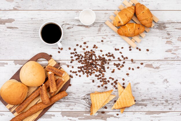 Vista superiore del pane della prima colazione con caffè sull'orizzontale di superficie di legno bianco