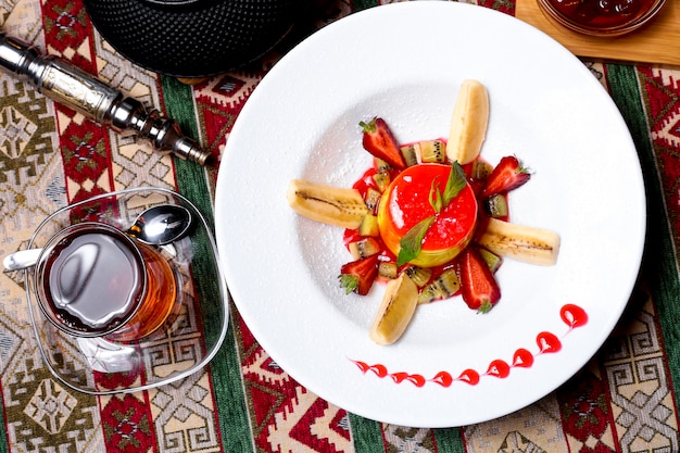 Vista superiore del piatto da dessert guarnito con fette di kiwi banana e fragole sciroppo di fragole