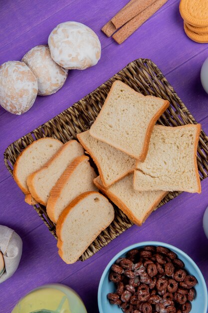 Vista superiore del piatto della merce nel carrello delle fette del pane bianco con i pan di zenzero dei cereali dei biscotti al latte condensato intorno sulla tavola porpora