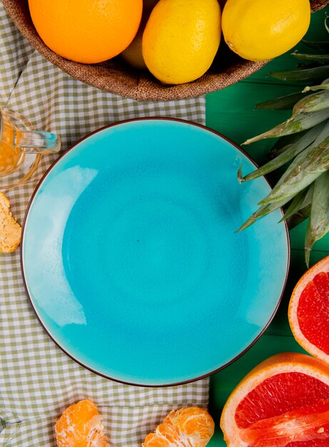 Vista superiore del piatto vuoto con gli agrumi come limone del pompelmo del mandarino intorno sul panno e sul fondo verde