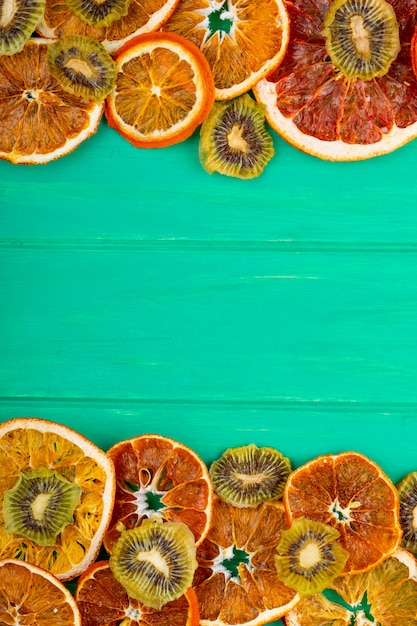 Vista superiore del pompelmo secco e delle fette arancio con il kiwi secco su fondo di legno verde con lo spazio della copia
