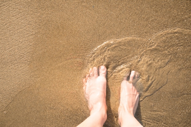 Vista superiore del primo piano dei piedi nella sabbia bagnata