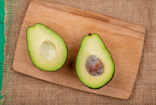 Vista superiore dell'avocado diviso in due sano e fresco su un bordo di legno della cucina sulla superficie del panno di sacco