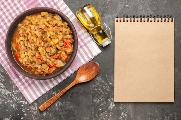 Vista superiore dell'insalata di melanzane arrosto nel blocco note dell'olio del cucchiaio di legno della ciotola sulla superficie scura