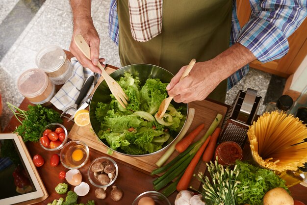 Vista superiore dell'uomo potato nell'insalata di miscelazione del grembiule del cuoco