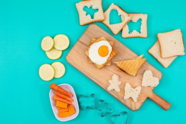 Vista superiore dell'uovo fritto con i pani tostati e le verdure sull'orizzontale di superficie del blu