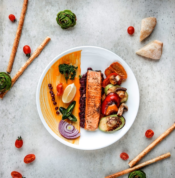 Vista superiore della bistecca di color salmone arrostita con il limone e le spezie delle verdure su un piatto bianco su bianco