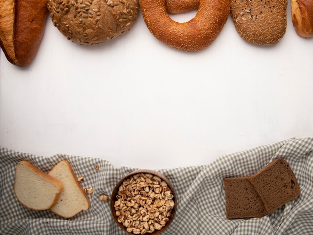 Vista superiore della ciotola con i semi e fette del pane di segale e bianche sul panno con altri pani su fondo bianco con lo spazio della copia