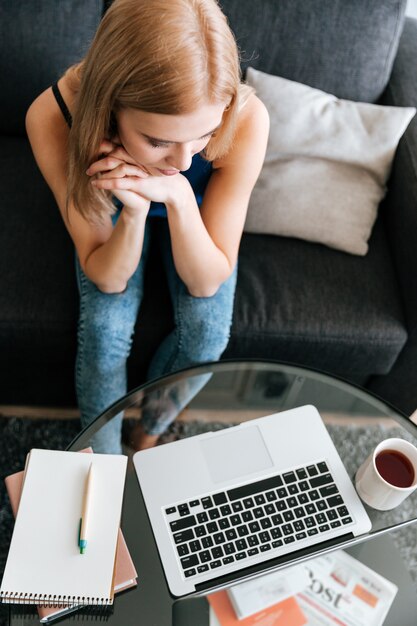 Vista superiore della donna pensierosa che lavora con il computer portatile a casa