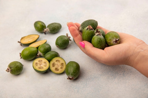 Vista superiore della mano femminile che tiene deliziosi feijoas freschi con feijoas isolati su un muro grigio