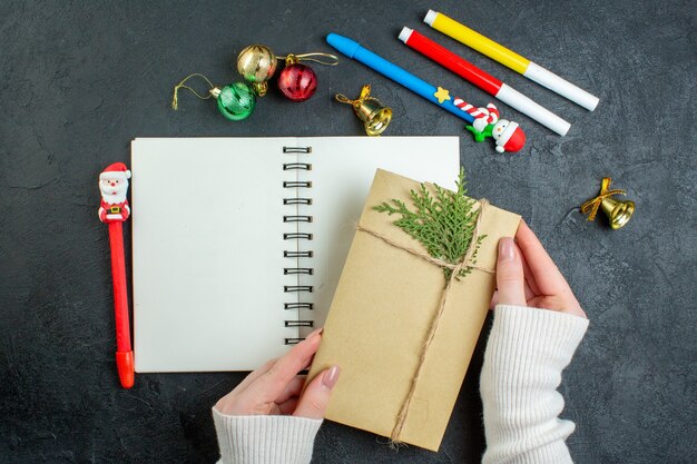 Vista superiore della mano un regalo sul taccuino a spirale con accessori per la decorazione di scrittura di felice anno nuovo su sfondo nero