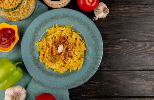 Vista superiore della pasta di maccheroni in zolla con ketchup, pepe, aglio e pomodoro sul panno blu e sulla superficie di legno con lo spazio della copia