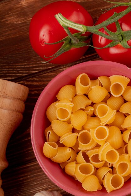 Vista superiore della pasta tubo-rigate in ciotola con pomodori e sale su superficie di legno