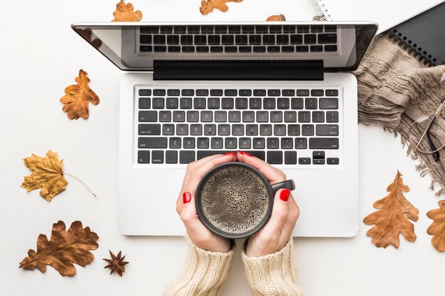 Vista superiore della persona che tiene la tazza di caffè con il computer portatile