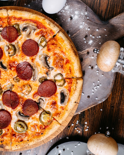 Vista superiore della pizza peperoni con funghi e peperoncini su un piatto di legno