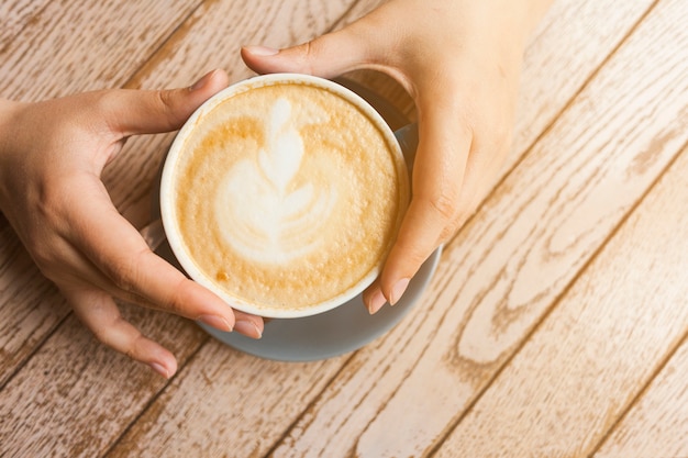 Vista superiore della tazza di caffè del latte della tenuta della mano umana sopra superficie di legno