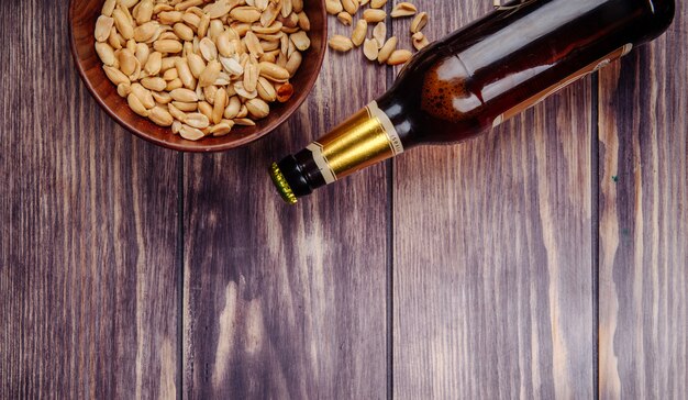 Vista superiore delle arachidi in una ciotola di legno con una bottiglia di birra su rustico con lo spazio della copia