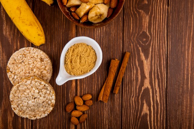 Vista superiore delle banane affettate con la mandorla in una ciotola di legno e le banane mature fresche con i cracker del riso e del cioccolato su legno