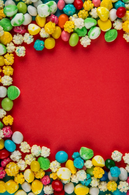 Vista superiore delle caramelle di zucchero dolci variopinte su fondo rosso con lo spazio della copia