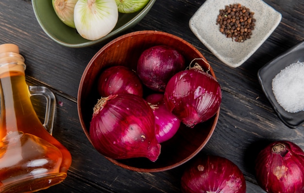 Vista superiore delle cipolle rosse in ciotola con la ciotola di cipolle bianche salate pepe nero pepe sale intorno su fondo di legno