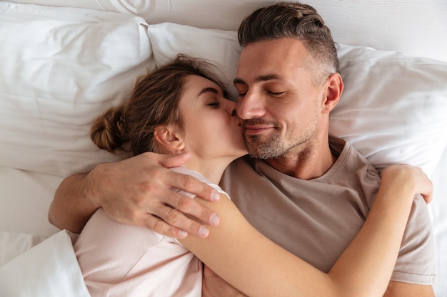 Vista superiore delle coppie amorose sensuali che si trovano insieme nel letto a casa mentre donna che bacia il suo ragazzo