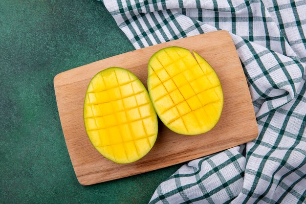 Vista superiore delle fette deliziose ed esotiche gialle del mango su un bordo di legno della cucina sulla tovaglia controllata e sulla superficie verde