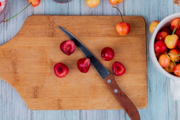 Vista superiore delle fette di ciliegia matura rossa su un tagliere di legno con un coltello da cucina su rustico