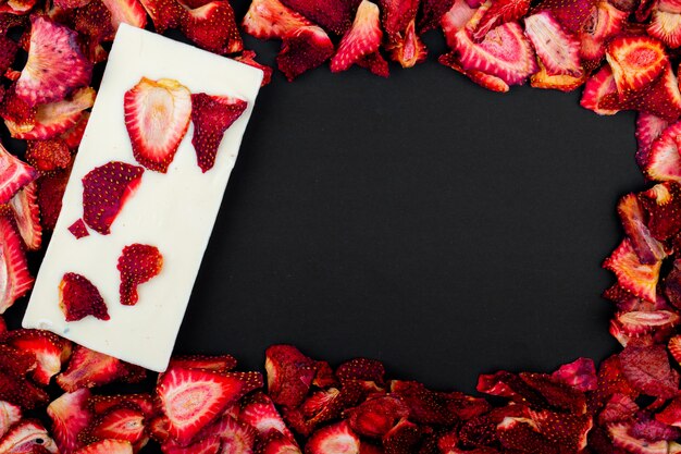 Vista superiore delle fette secche della fragola con la barra di cioccolata bianca su fondo nero