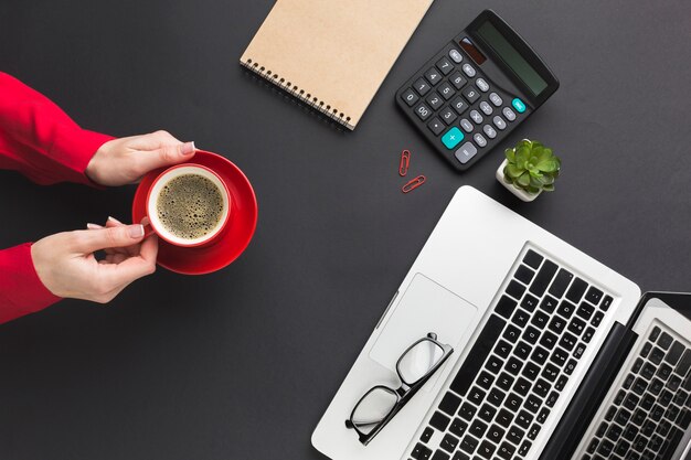 Vista superiore delle mani che tengono la tazza di caffè sullo scrittorio del lavoro