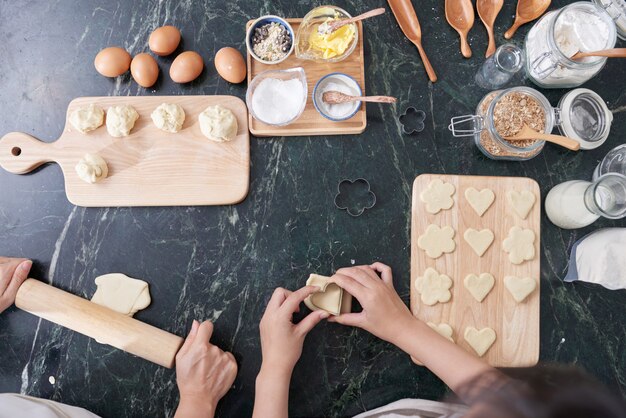 Vista superiore delle mani di due persone che cucinano insieme biscotti fatti in casa