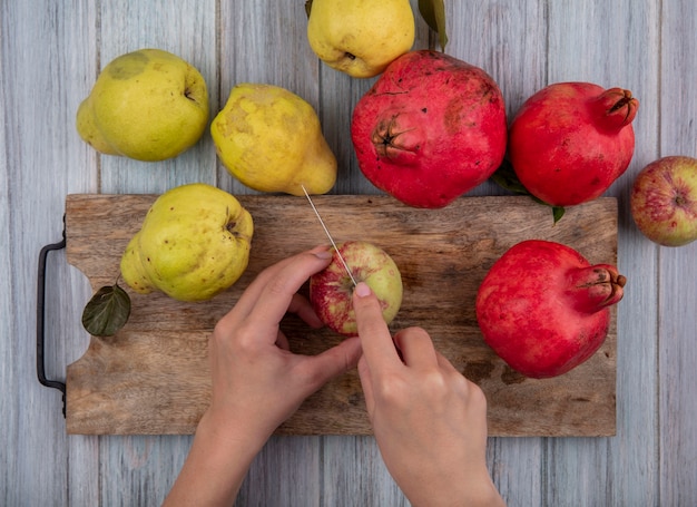 Vista superiore delle mani femminili che tagliano la mela fresca su una tavola di cucina in legno con il coltello su un fondo di legno grigio