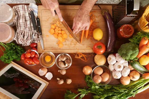 Vista superiore delle mani potate della carota di taglio irriconoscibile del cuoco senior che cucina stufato di verdure