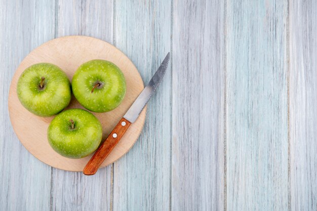 Vista superiore delle mele deliziose fresche verdi su un bordo della cucina di taglio con il coltello su superficie di legno grigia