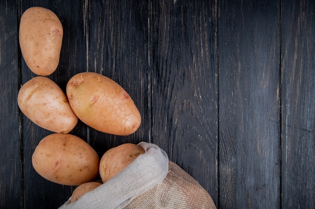 Vista superiore delle patate che si rovesciano dal sacco su superficie di legno con lo spazio della copia