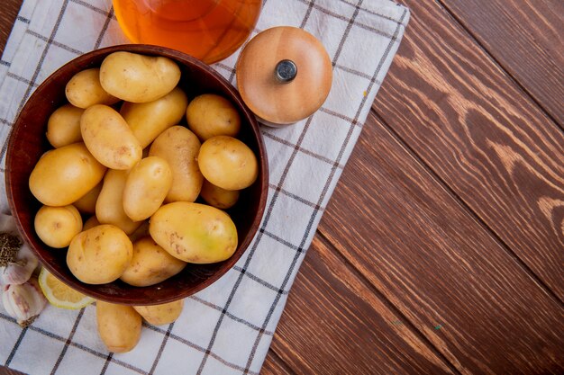 Vista superiore delle patate in ciotola con sale e burro di limone dell'aglio sul panno e sul legno del plaid con lo spazio della copia