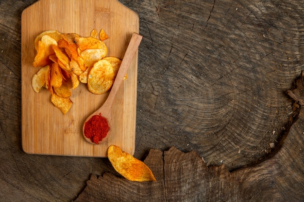 Vista superiore delle patatine fritte con un cucchiaio di legno di polvere di peperoncino su un tagliere di legno con lo spazio della copia