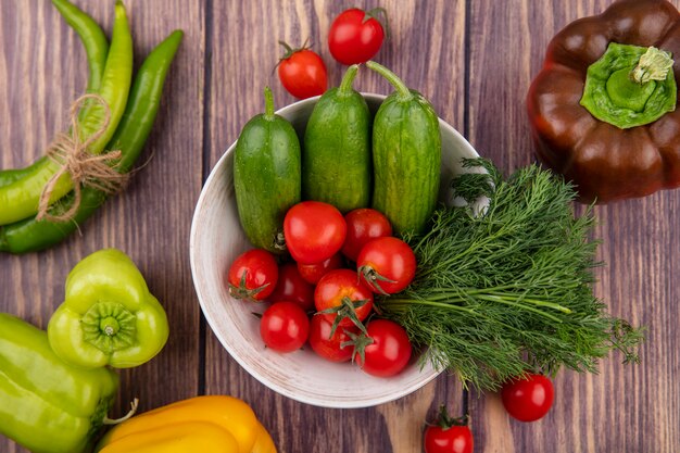 Vista superiore delle verdure come aneto del cetriolo del pomodoro in ciotola con i peperoni su superficie di legno