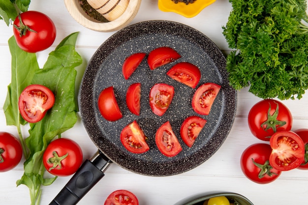 Vista superiore delle verdure come coriandolo degli spinaci del pomodoro con le fette del pomodoro in padella su legno