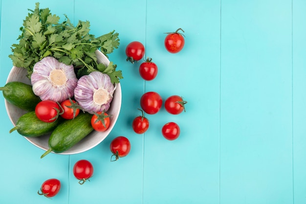 Vista superiore delle verdure come coriandolo ed aglio del cetriolo del pomodoro in ciotola sulla superficie del blu