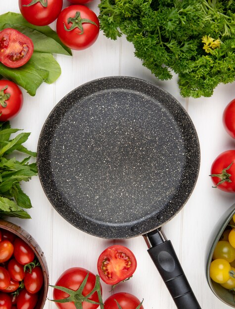 Vista superiore delle verdure come foglie di menta verdi degli spinaci del coriandolo del pomodoro con la padella sul centro su superficie di legno