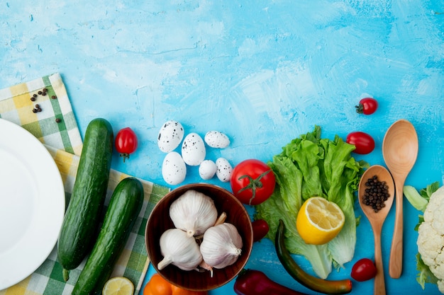 Vista superiore delle verdure come lattuga di uova dell'aglio del cetriolo ed altre con lo spazio del pepe e del limone su fondo blu con lo spazio della copia