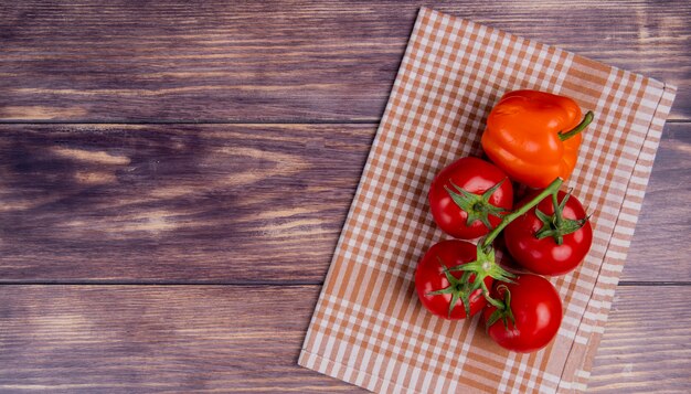 Vista superiore delle verdure come pepe e pomodori sul panno del plaid dalla destra e superficie di legno con lo spazio della copia