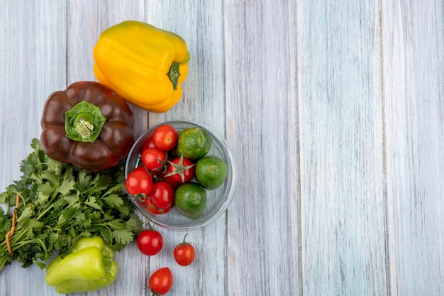 Vista superiore delle verdure come pomodoro e cetriolo in ciotola con pepe e mazzo di coriandolo su superficie di legno