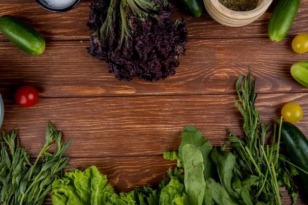 Vista superiore delle verdure come spinaci della lattuga alla menta del basilico del pomodoro del cetriolo con il sale del pepe nero su legno