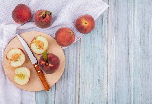 Vista superiore di mezze pesche sul bordo della cucina di taglio con coltello con pesche isolato su superficie di legno grigio