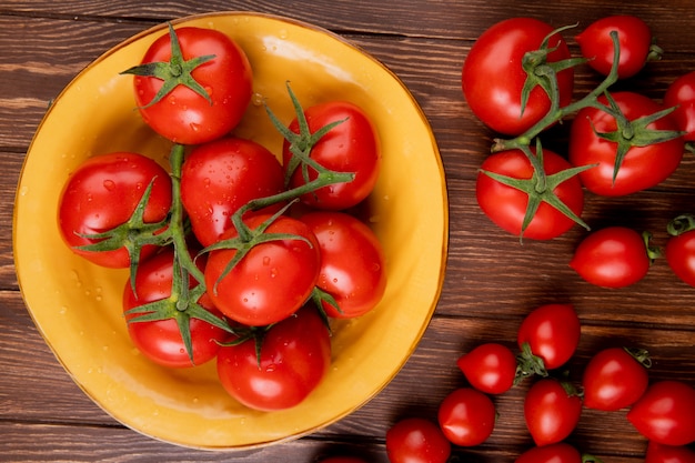 Vista superiore di pomodori in ciotola e altri pomodori su superficie di legno