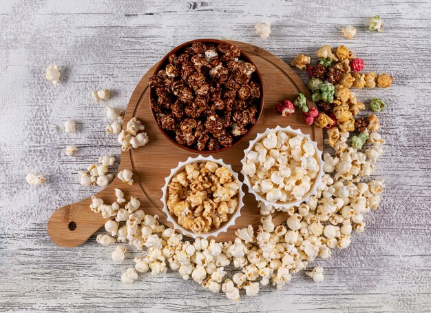 Vista superiore di popcorn in ciotole e tagliere di legno sull'orizzontale bianco